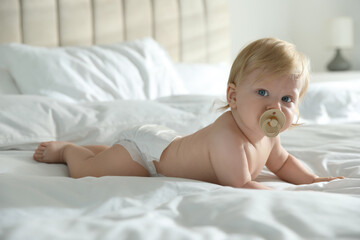 Cute little baby in diaper with pacifier lying on bed at home