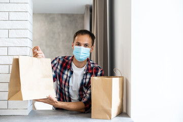 Delivery man holding a paper bag with food. Man delivering food in disposable paper bag to customer home with facemask. Delivery in time of coronavirus