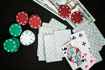 Casino poker chips stack with playing cards, dice and money on green felt background.