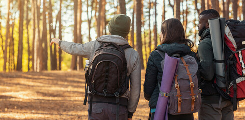 Friends hikers walking by forest, guy pointing at copy space