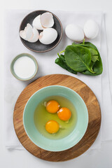 The process of making tasty egg omelet with green spinach leaves for breakfast on a white background. Top view. Idea recipe for a healthy diet food. Easy to cook. Protein food for a vegetarian.