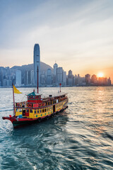 Naklejka premium Tourist boat crossing Victoria Harbor in Hong Kong at sunset