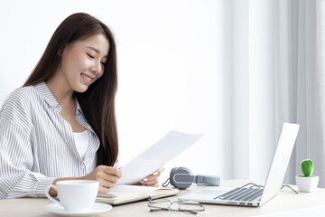 Young Asian woman works on paperwork in her own home online.