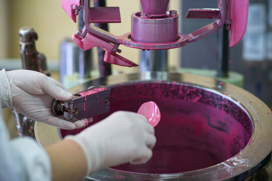 Manufacturing paint in a factory. Pink colored paint in an industrial environment.  A worker wearing rubber gloves working with liquids
