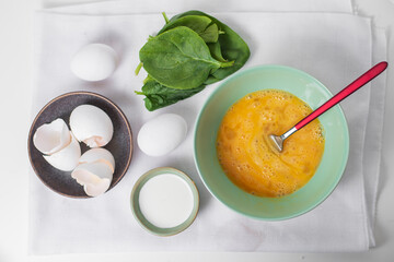 The process of making tasty egg omelet with green spinach leaves for breakfast on a white background. Top view. Idea recipe for a healthy diet food. Easy to cook. Protein food for a vegetarian.