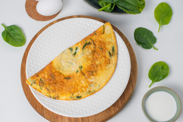 Tasty homemade omelet with green leaves spinach on a white background. Top view. Idea recipe for a healthy diet breakfast. Concept of losing weight. Easy to cook. Protein for a vegetarian.