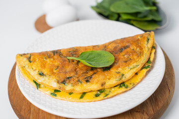 Tasty homemade omelet with green leaves spinach on a white background. Close up. Idea recipe for a healthy diet breakfast. Concept of losing weight. Easy to cook. Selective focus.