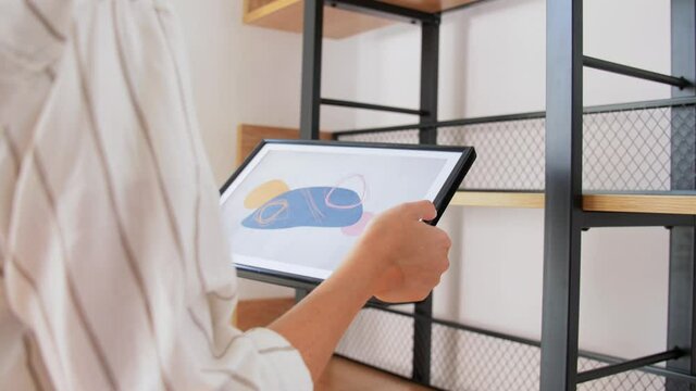 home improvement, decoration and people concept - woman placing picture in frame to shelf