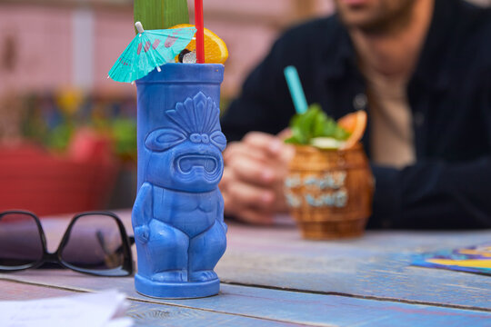 Tropical cocktail with orange in blue tiki style glass on wooden background