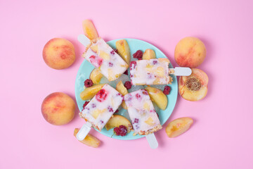 fresh summer ice cream on a stick with peach and raspberry berries on a pink background top view . ice cream ingredients ripe peaches and raspberries with yogurt