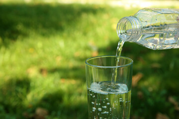 Pouring water from bottle into glass and blurred green grass on background. Space for text