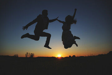 Fototapeta na wymiar silhouette of young couple are jumping and having fun outdoors in the field on summer evening. romantic photo at sunset time. love story