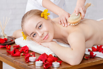 Obraz na płótnie Canvas Massage with brush. Smiling girl receives massage on massage table with rose petals