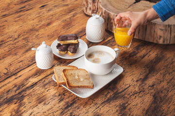 Woman placing an orange juice transparent crystal glass on vintage wooden table beside a withe porcelain milk cup on a white tray with toast and honey
