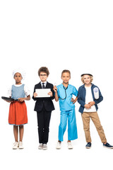 Fototapeta premium multicultural children in costumes of different professions holding frying pan, blueprint, stethoscope and digital tablet isolated on white