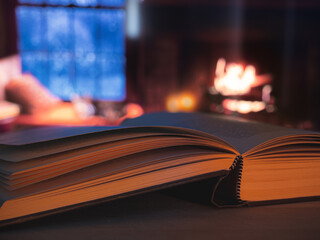 An open hardback book lit by candles and a roaring log fire in a cabin