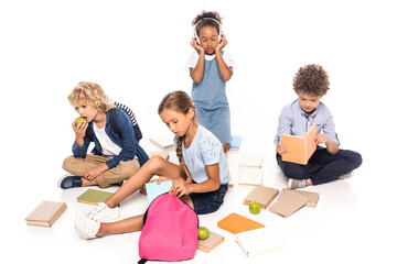schoolkids sitting near books, apples and african american child in wireless headphones isolated on white