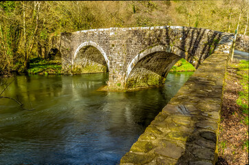 Fototapeta na wymiar The river bank wall leads up to the Llawhaden bridge, an eighteenth-century, grade 2 listed bridge that spans the River Cleddau, Wales