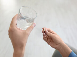 Woman holding glass of water and pill at home, closeup