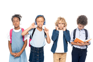 multicultural schoolkids listening music in wireless headphones near curly boy reading book isolated on white