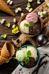 Different scoops of Vanilla pistachio chocolate and strawberry icecream balls in clay bowls on wooden kitchen table. Flat lay