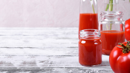 Tomato juice in glass jars on white wooden table. Copy space