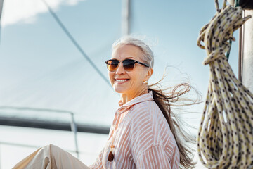 Portrait of a happy mature woman wearing sunglasses on a yacht. Beautiful female with long hair...