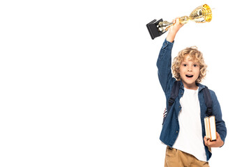 excited blonde schoolboy holding golden trophy and books isolated on white