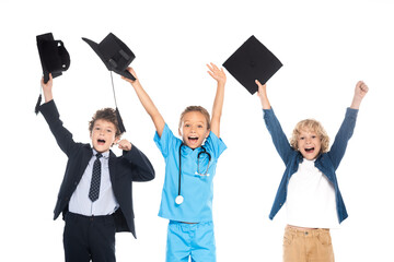 excited children dressed in costumes of different professions holding black graduation caps above heads isolated on white