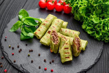 Thin pancakes with spinach and meat on a black background