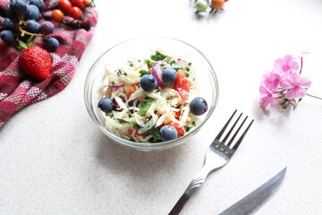 Use of various berries and fruits in the preparation of vegetable salads-grape berries in cabbage salad in a glass dish on the kitchen table, fork and napkin with berries-side view