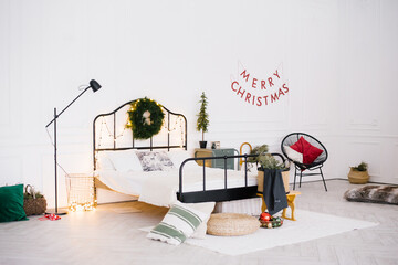 White stylish cozy scandinavian bedroom. New year winter home interior decor. Christmas holiday decorations: little christmas tree, wreath, led garland lights.