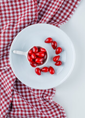 Cornel berries in scoop and plate on white and picnic cloth background. top view.
