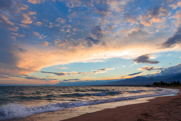 Beautiful sunset by the lake. Bright clouds are reflected in the water. Kyrgyzstan.