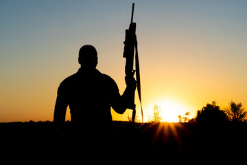 Silhouette of a man with a weapon in his hands on a sunset background