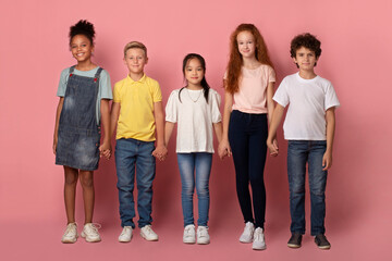 Obraz premium School friendship. Adorable multiethnic children holding hands together over pink background