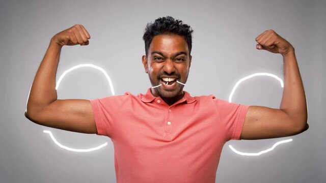 power, strength, sport and people concept - happy young indian man showing biceps over grey background with animated glowing lines
