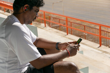 Runner man using smartphone after finished pratice or run. Sitting at stadium