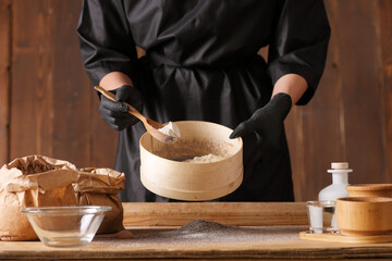 Cook hands kneading dough, sprinkling piece of dough with white wheat flour. Low key shot, close up on hands, some ingredients around on table.