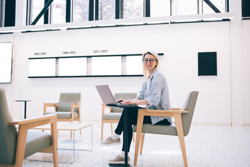 Cheerful young freelance woman using laptop in business center