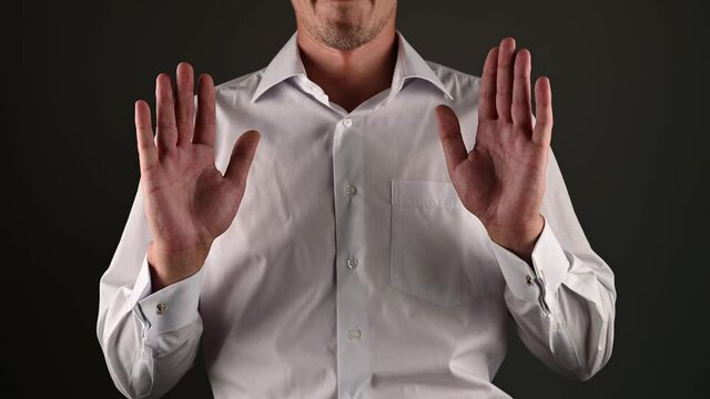 A man in a white shirt raises his hands surrendering. on a dark background