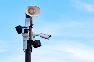 Security cameras and speakers on a pole above a blue sky. Close-up of outdoor surveillance cameras, floodlights and loudspeakers on a street pole. Ensuring security on the street.