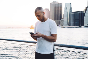 Young ethnic man listening to music in earphones near river