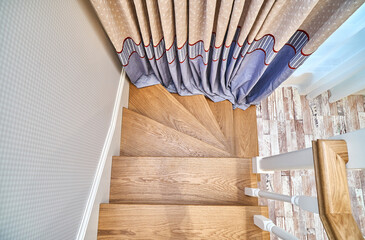 Winder steps of a wooden staircase with white balusters. View from above