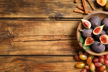 Tasty fresh figs, cinnamon and grapes on wooden table, flat lay. Space for text