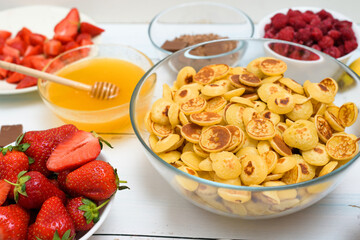 mini pancake cereal bowl with fresh strawberries banana chocolate, coconut shavings and honey in small plates. the view from the top . the trend of self-isolation