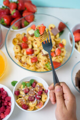 tiny pancakes on a fork with fresh strawberries, banana, chocolate, coconut chips and honey in a plate on a blue background. food trend 2020