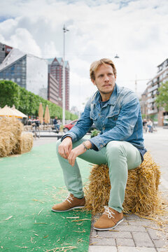 Young man sitting on a hay bale with a straw in his mouth