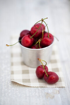Two cherries in front of steel can filled with fresh cherries on cotton checked fabric