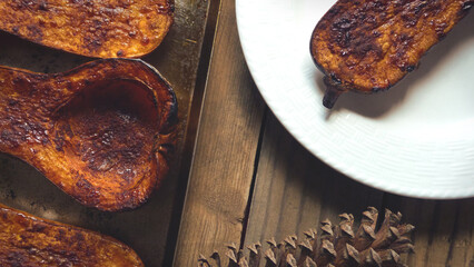 Baked Butternut Squash on a Cooking Sheet by a Plate and Pine Cone on a Wood Surface | Rustic Kitchen